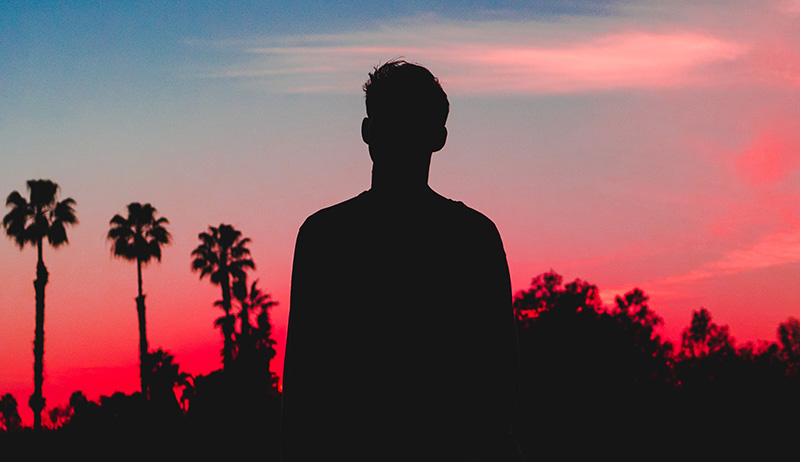 Boy before palms at sunset