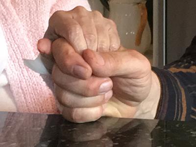 Elderly woman's hand held in a younger man's hand in prayer