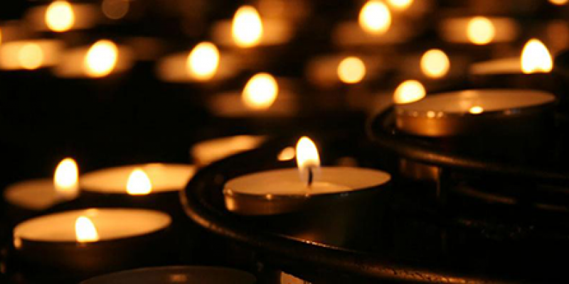 Many small votive candles with flames burning bright in the dark